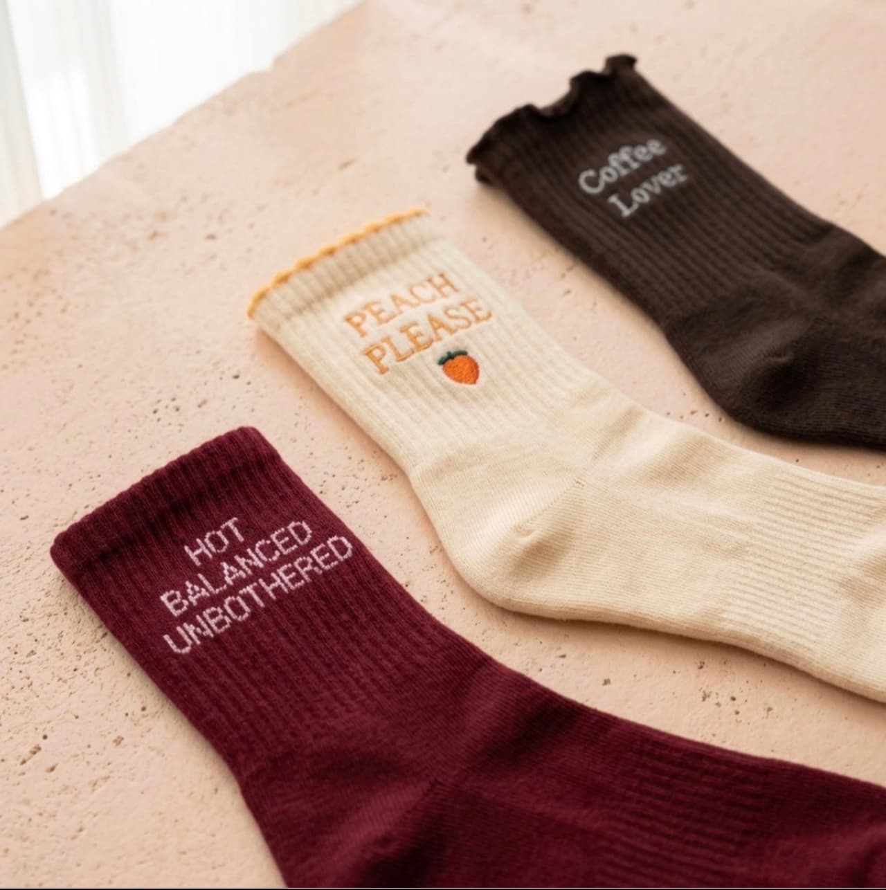 Drei stylische Crew Grip Socks in Bordeaux, Orange und Dunkelbraun mit verschiedenen Schriftzügen und Designs auf einer hellen Oberfläche.