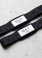 Schwarze Zughilfen von NST Fitness mit grauem Wabenmuster und weißem Logo-Label für Krafttraining und Gewichtheben.