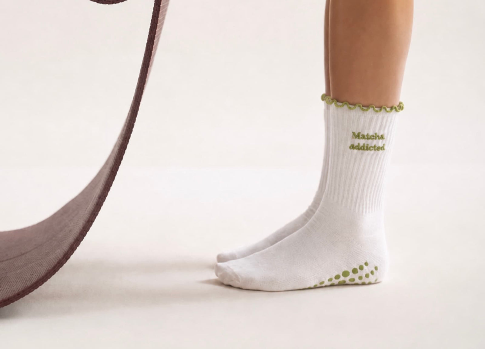 Weiße Grip-Socken mit grünem „Matcha addicted“-Schriftzug und grünen Grip-Noppen an der Sohle, getragen bei einer Pilates-Übung am Reformer.