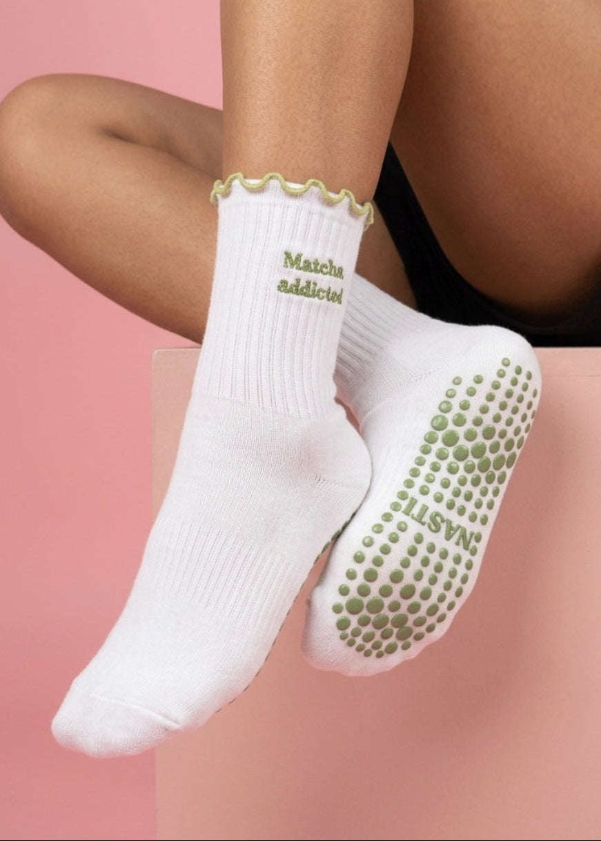 Weiße Pilates Socken mit einem grünen Rüschenrand und einer Schrift die sagt "Matcha Addicted". Grüne gepunktete Noppen auf der Sohle