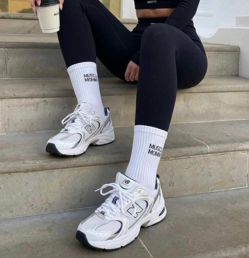Frau in schwarzem Gym-Outfit mit weißen Sportsocken und weißen Sneakern auf einer Treppe