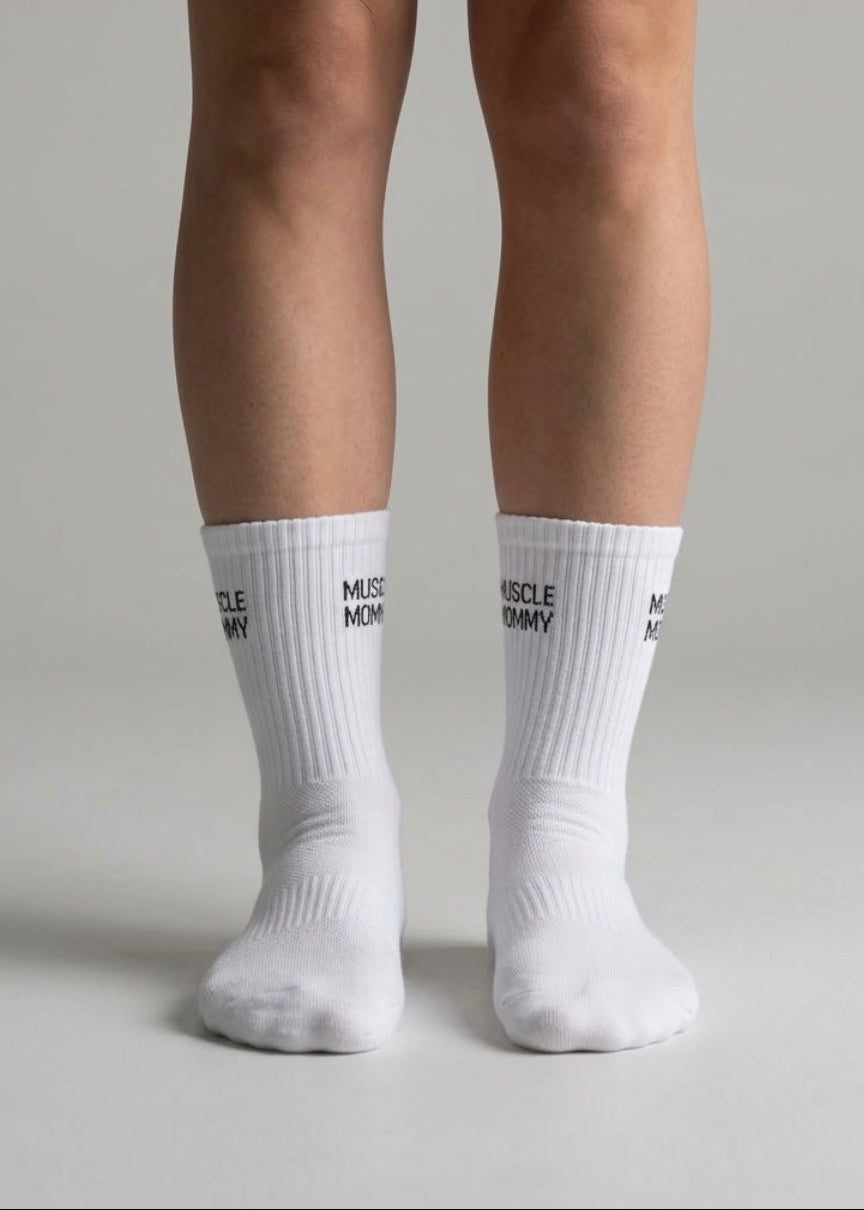 Weiße Sportsocken mit schwarzem „Muscle Mommy“-Schriftzug an beiden Beinen einer Person