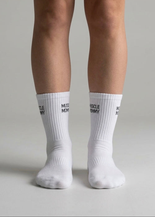 Weiße Sportsocken mit schwarzem „Muscle Mommy“-Schriftzug an beiden Beinen einer Person
