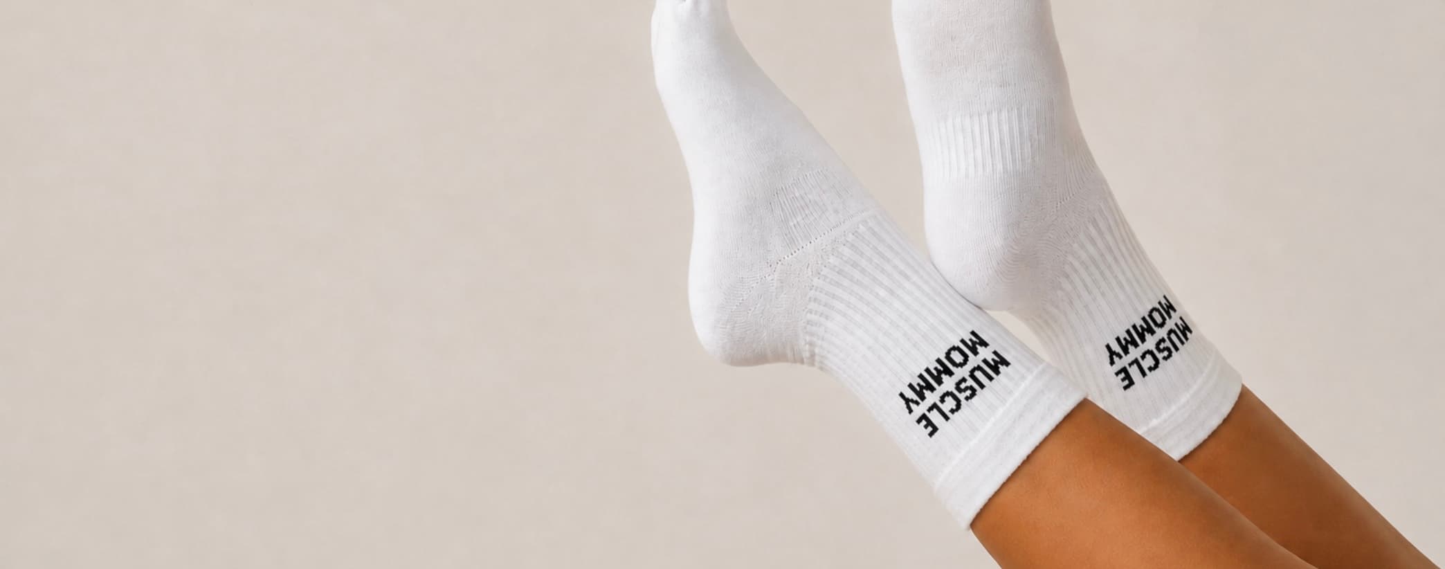 Weiße Pilates-Socken an zwei Beinen vor hellem Hintergrund, mit schwarzem „MUSCLE MOMMY“-Schriftzug am Bündchen.