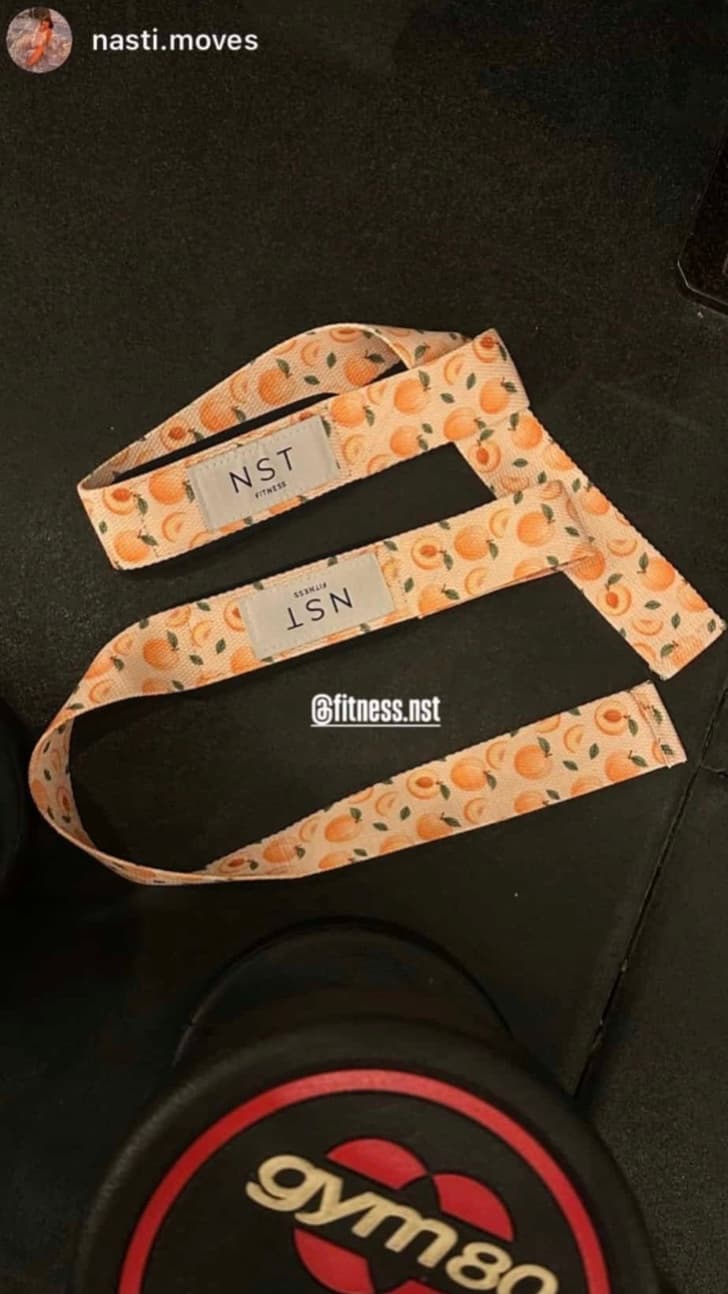 NST Fitness Zughilfen mit orangefarbenem Pfirsichmuster auf einer schwarzen Trainingsbank im Gym, mit gepolsterten Handgelenkschlaufen für mehr Halt beim Krafttraining.