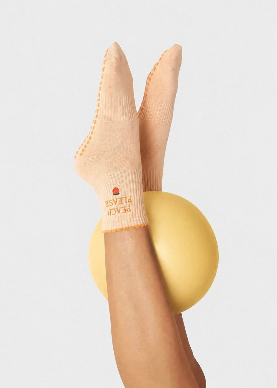 Orangene Pilates Socken mit einem gelben Ball zwischen den Knöcheln