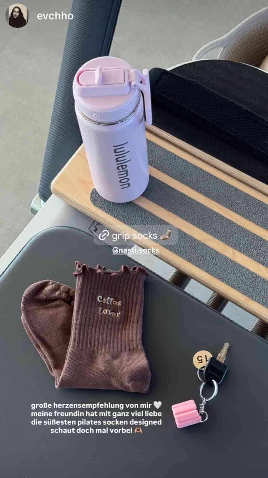 Braune NST Grip Socks mit „Coffee Lover“-Schriftzug und rutschfesten Noppen liegen auf einem Pilates-Reformer neben einer Trinkflasche und einem Schlüsselbund.