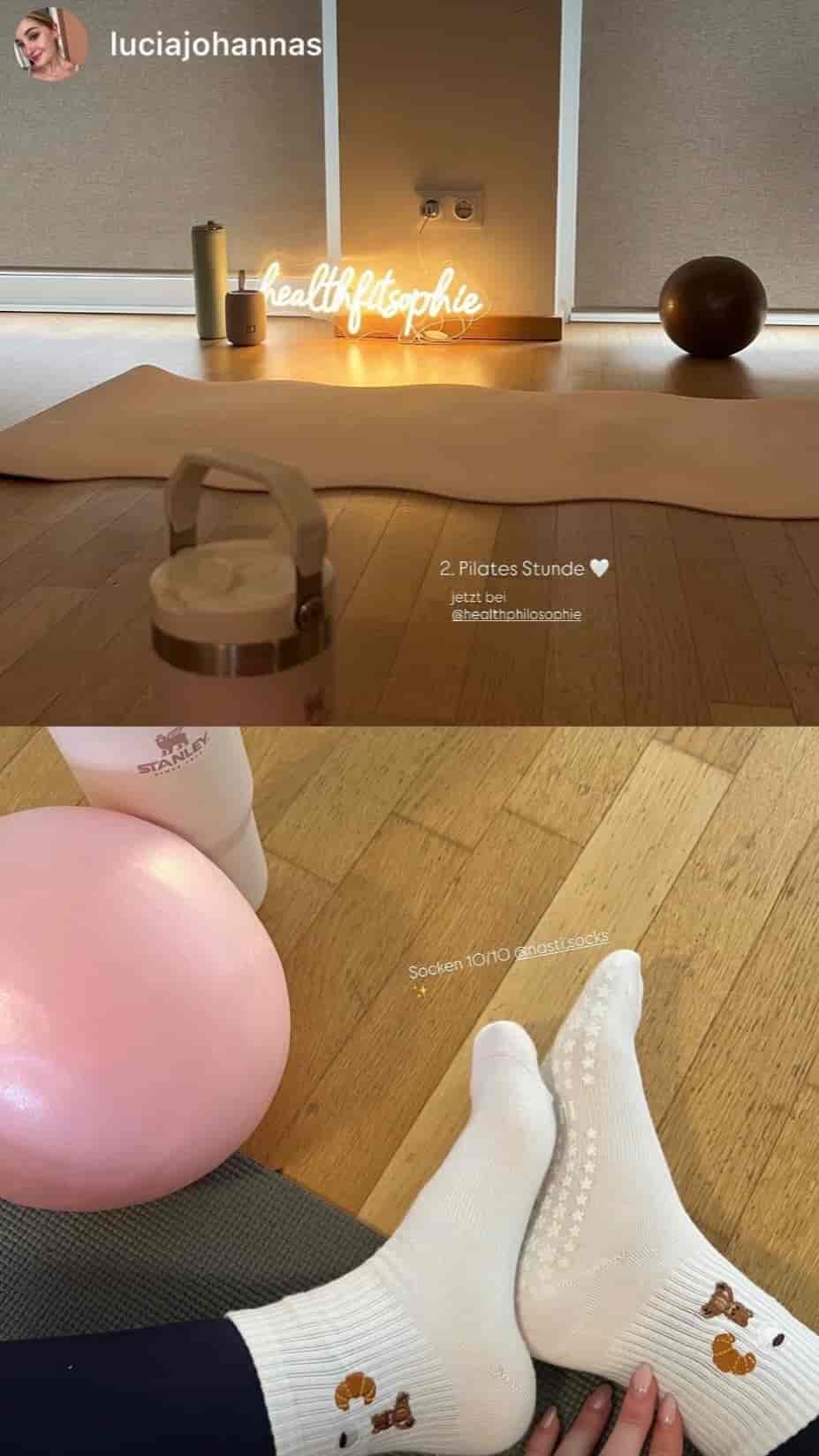 Pilates-Setup mit Yogamatte, Pilates-Ball und Trinkflasche; im Vordergrund trägt eine Person weiße Pilates-Socken mit Blumen- und Schmetterlingsmotiv sowie rutschfesten Sohlen.