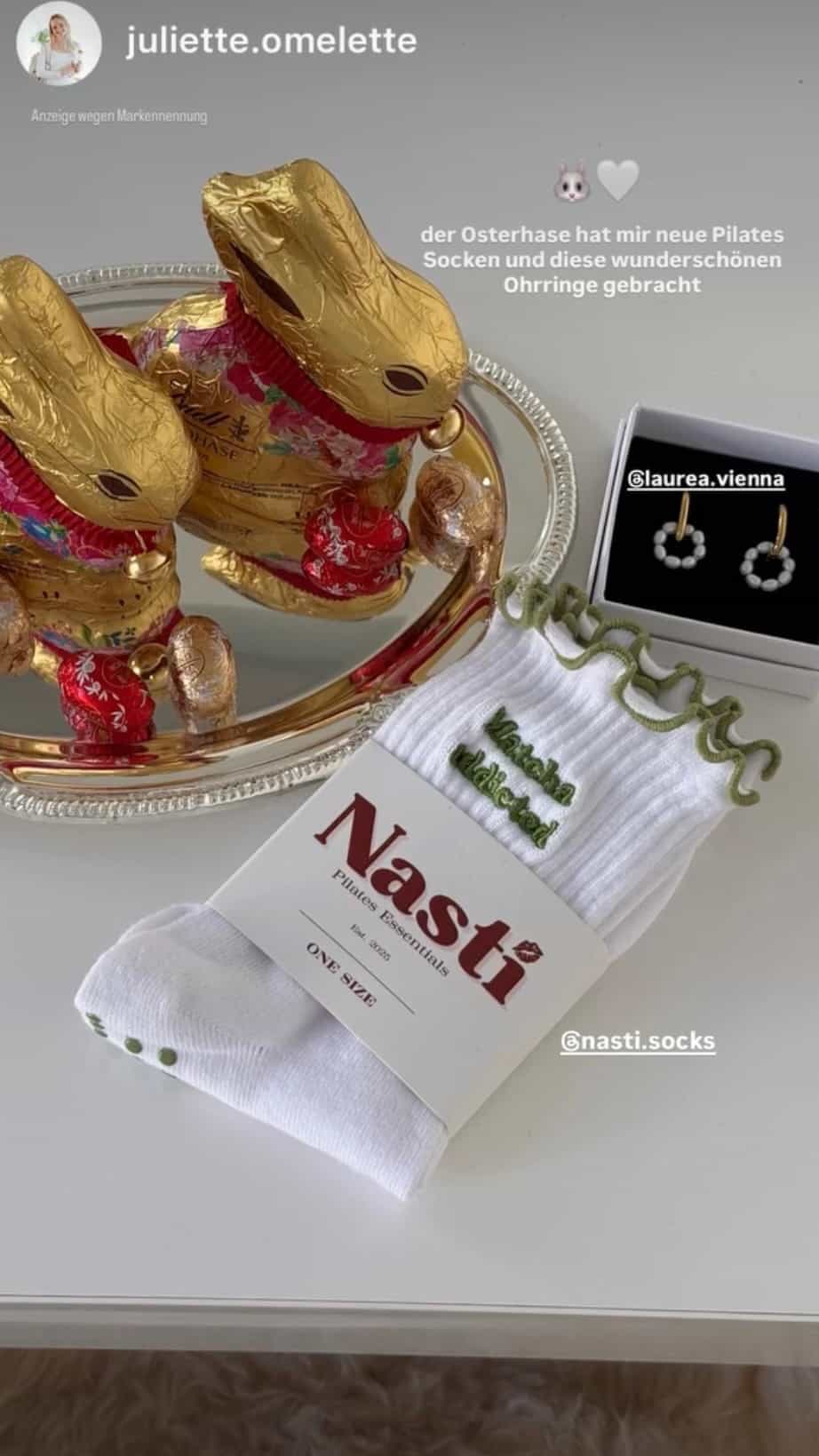 Weiße Pilates Grip Socken mit grünem Schriftzug und rutschfesten Noppen, präsentiert neben Osterhasen und Ohrringen – NST Socks Pilates Socken.