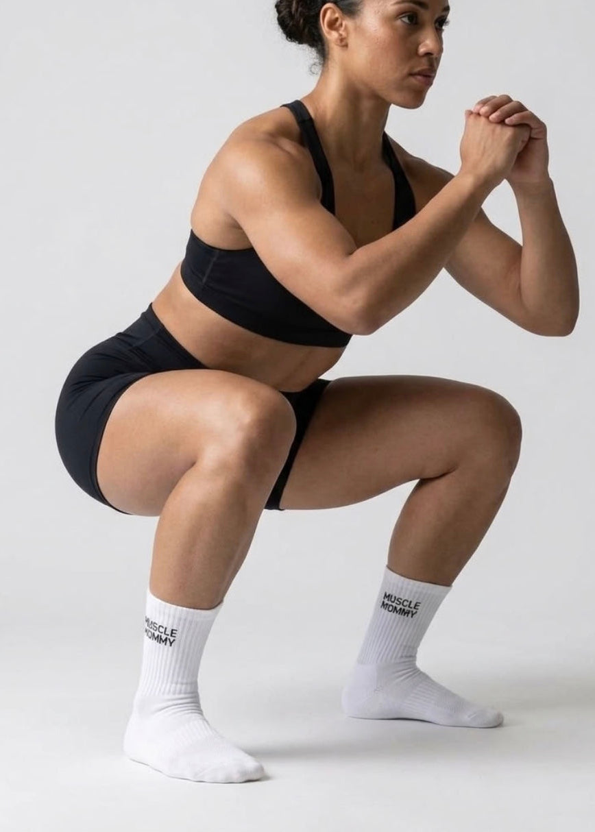 Eine Frau die eine Kniebeuge ausführt udn dabei weiße Sportsocken trägt