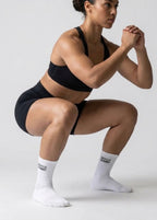 Eine Frau die eine Kniebeuge ausführt udn dabei weiße Sportsocken trägt