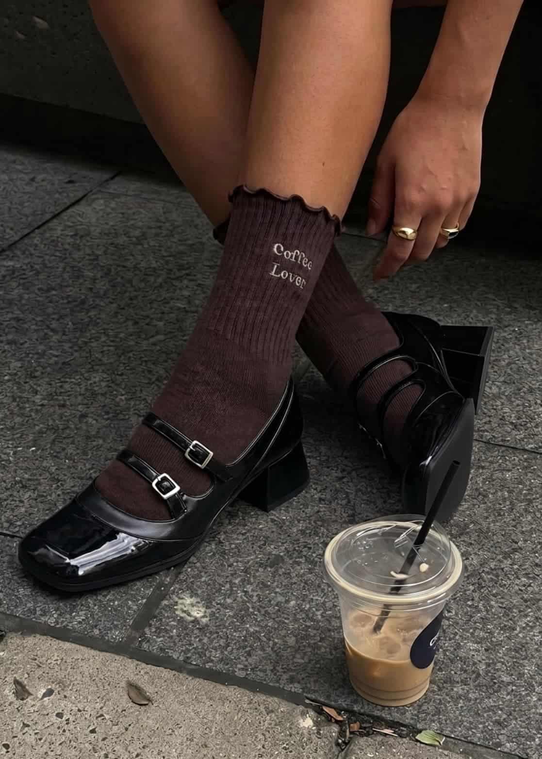 Braune Pilates Socken in schwarzen Schuhe. Daneben liegt ein Kaffee auf den boden