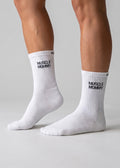 Weiße Performance-Sportsocken mit schwarzem „Muscle Mommy“-Schriftzug an den Füßen einer Person.