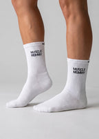 Weiße Performance-Sportsocken mit schwarzem „Muscle Mommy“-Schriftzug an den Füßen einer Person.