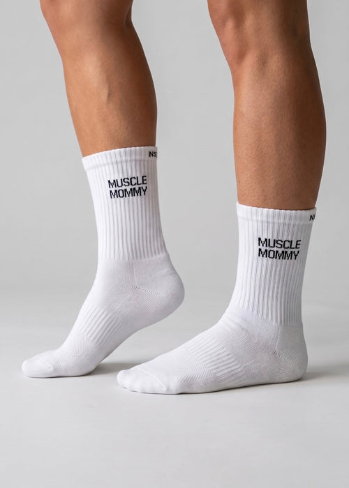 Weiße Performance-Sportsocken mit schwarzem „Muscle Mommy“-Schriftzug an den Füßen einer Person.
