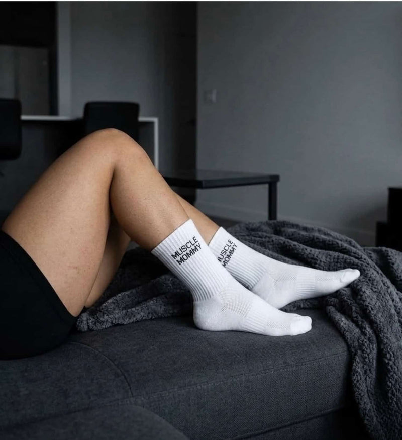 Weiße Sportsocken für Damen mit Muscle Mommy Schriftzug und atmungsaktivem Mesh am Fuß, entspannt auf dem Sofa getragen