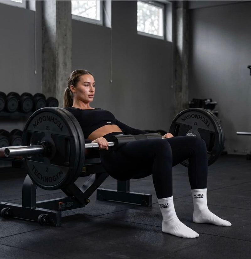 Frau beim schweren Hip Thrust im Gym mit weißen Sportsocken für Damen von NST mit dem Schriftzug Muscle Mommy