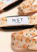 NST Fitness Zughilfen mit orangefarbenem Orangen-Print und Logo auf hellem Hintergrund – stylische Zughilfen fürs Krafttraining im Gym.